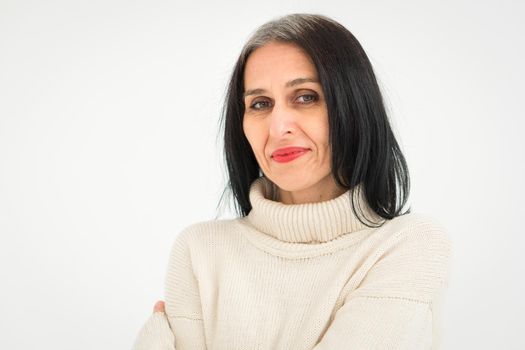 Middle aged woman starting getting grey-haired is posing in studio in sweater on white background, face skin care beauty, middle age skincare cosmetics, cosmetology concept.