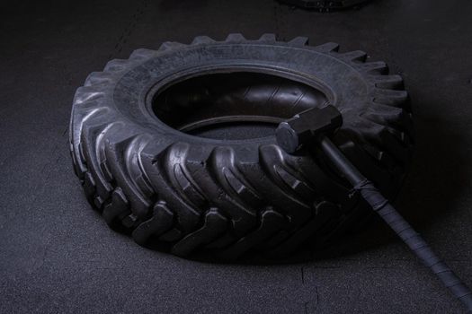 A tire on a black background with a sledgehammer lies for crosfit fitness wheel sledgehammer workout body sport, In the afternoon athlete exercise from lifestyle heavy effort, athletic build. Sweat indoors diet,
