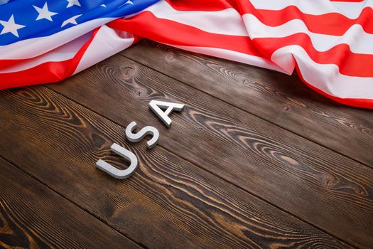the word USA laid with silver metal letters on wooden board surface under crumpled flag of United States of America in diagonal slanted perspective