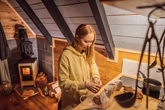 Young woman cooking food whilst glamping. Rest in the mountains in Glamping. Cozy fireplace in a mountain house.