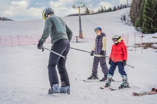 Mom and son are learning to ski with an instructor.Active toddler kid with safety helmet, goggles and poles. Ski race for young children. Winter sport for family. Kids ski lesson in alpine school. Little skier racing in snow.