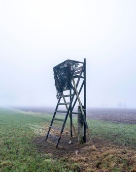 high seat for hunting in green grass of winter field near utrecht in the netherlands on misty winter day
