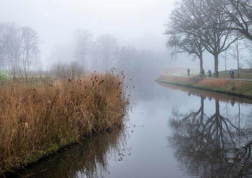 valleikanaal or valley canal and rtow of bikes near scherpenzeel in dutch province of utrecht on misty winter day