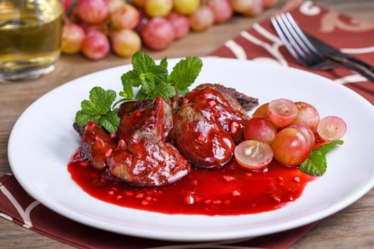 Warm salad with chicken liver and grapes on the plate. Warm salad from turkey liver. Warm salad with chicken liver in raspberry sauce.