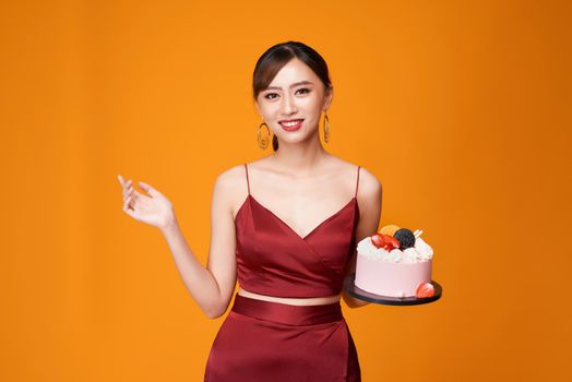 Vertical shot of an elegant woman in a red dress carrying a birthday cake