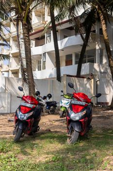 Negombo Sri Lanka - december 5 2021: Motorbikes stand under palm trees on the grass near the white house with balconies, built next to the seashore. High quality photo