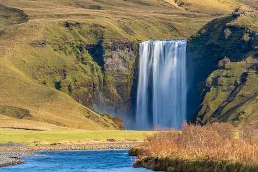 Long exposure of famous Skogafoss waterfall in Iceland from the distance with hikers on top viewpoint