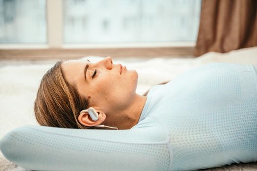 Side view portrait of relaxed woman listening to music with headphones lying on carpet at home. She is dressed in a blue tracksuit