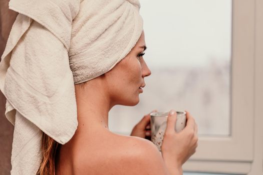 Young serene relaxed woman in spa bath towel drinking hot beverage tea coffee after taking shower bath at home. Beauty treatment, hydration concept