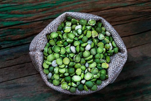 split peas in a burlap bag with a wooden scoop on a white background