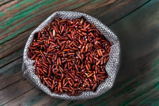 Grains of red rice in a macro shown in burlap bag on a green background