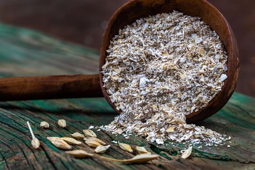 Wooden spoon filled with oatmeal next to oat grains