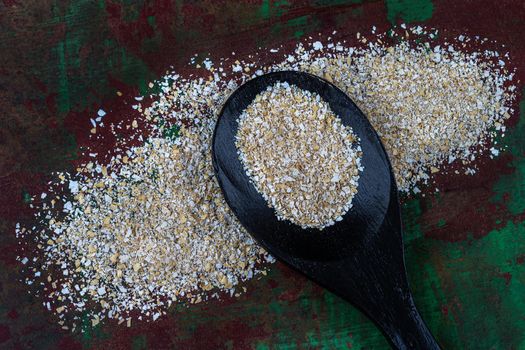 Wooden spoon filled with oatmeal next to oat grains