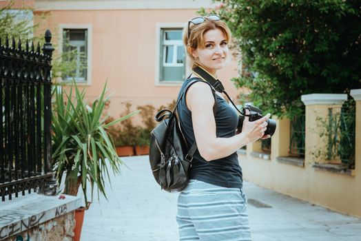 Beautiful girl walking along the street of an old European town with a film camera in her hand. Portrait of a tourist girl walking on the street background