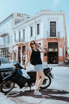 Beautiful girl walking along the street of an old European town with a film camera in her hand. Portrait of a tourist girl walking on the street background