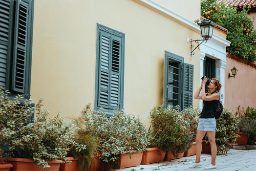 Beautiful girl walking along the street of an old European town with a film camera in her hand. Portrait of a tourist girl walking on the street background