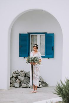 Handsome beautiful caucasian bride posing near white wall with blue windows. Young attractive bride with the bouquet of flowers.