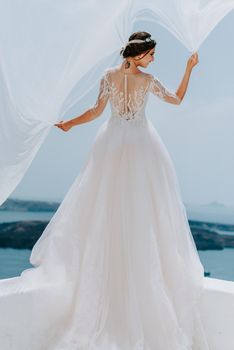 Romantic beautiful bride in white dress posing on terrace with sea and mountains in background