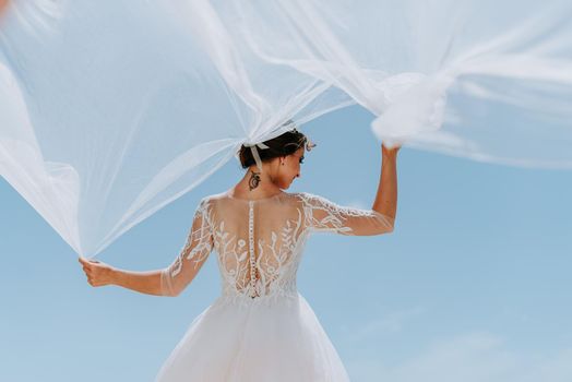 tender young bride against the blue sky and ocean. she keeps at hands waving in the wind veil