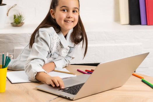 Little girl doing her homework at home and using a laptop
