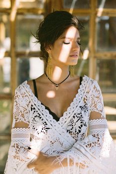 Girl in a white dress sits against the background of a wooden window, closing her eyes. High quality photo