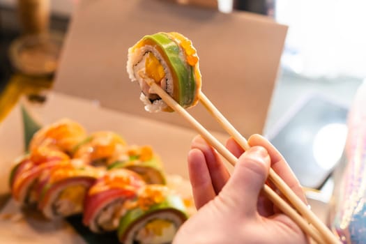 close up of chopsticks taking portion of sushi roll on the table restaurant. eating sushi roll using chopsticks.