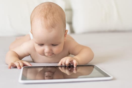 A six-month baby with a tablet computer, looking at screen, at home.