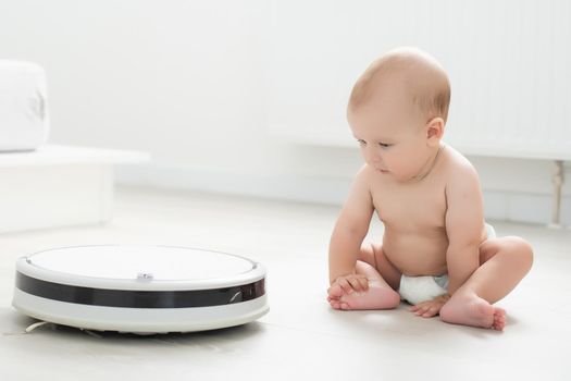 little baby on flour playing with robot vacuum cleaner at home. Happy family moving to new apartment.