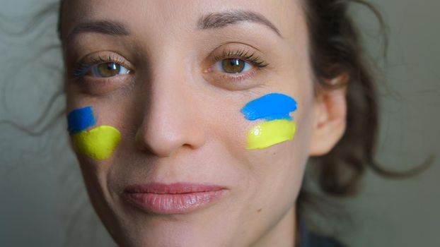 Indoor portrait of young girl with blue and yellow ukrainian flag on her cheek wearing military uniform, mandatory conscription in Ukraine, equality concepts.