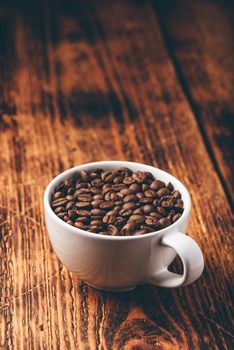 Roasted coffee beans in white cup over rustic wooden surface