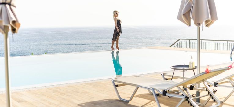 An attractive young woman stands near the pool with a panoramic view.