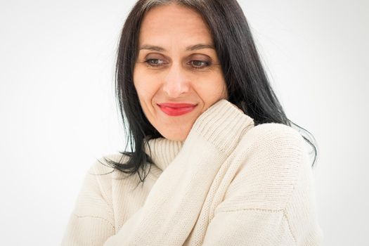 Middle aged woman starting getting grey-haired is posing in studio in sweater on white background, face skin care beauty, middle age skincare cosmetics, cosmetology concept.