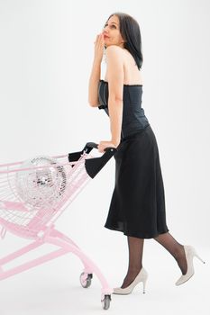 Studio photo of middle aged woman starting getting grey-haired wearing black clothes with silver disco ball in shopping basket white background, middle age sexy lady, happy life concept.