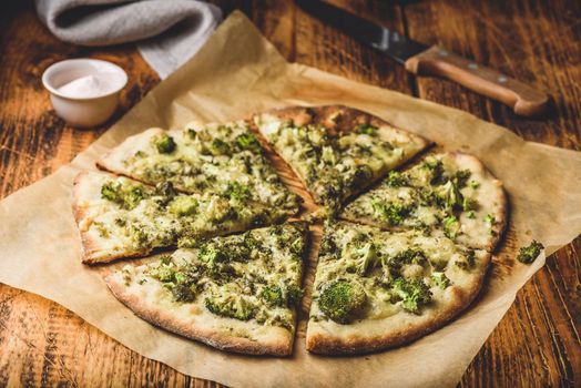 Sliced homemade pizza with broccoli, pesto sauce, spices and cheese on baking paper