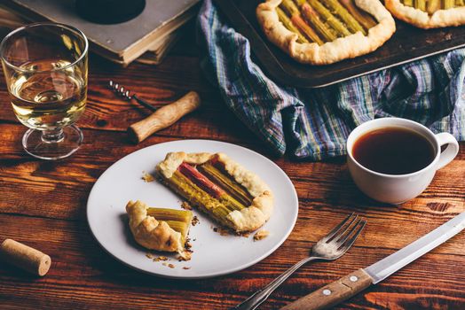 Fresh baked rhubarb mini galette on white plate with glass of white wine and cup of coffee