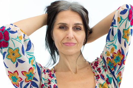 Close-up portrait of middle aged woman starting getting grey-haired wearing dress with flowers on white background, middle age sexy lady, cosmetology concept.