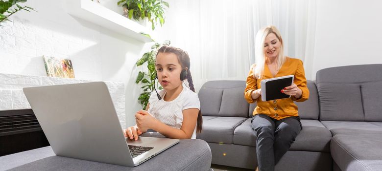 smiling young mother and daughter studying online classes in home office in the modern living room