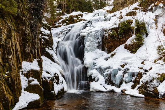 Long high waterfall in mountains full of snow and ice around