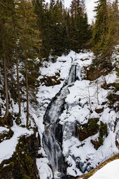 Long high waterfall in mountains full of snow and ice around