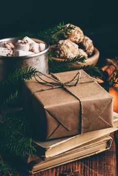Gift box wrapped with craft paper on stack of old books. Hot chocolate, spices and fruits