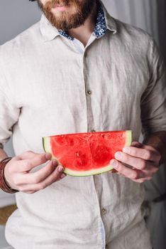 Bearded man in linen shirt holds in his hands slice of ripe red watermelon