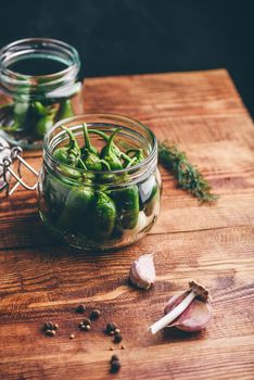 Jalapeno Peppers in a Glass Jars for Canning with Garlic and Peppercorns on Wooden Table