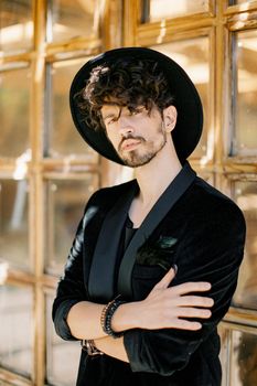 Young man in a black hat stands with his arms crossed against the background of a wooden window. High quality photo