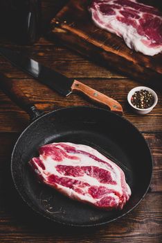 Raw pork neck steak in cast iron skillet