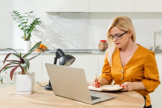 Remote working from home. Young woman using laptop. Freelancer workplace in kitchen office. Teleworking in isolation, female business, shopping online. Student in distance learning. Lifestyle moment.