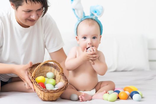 happy family celebrating easter mother and baby bunny ears at home with colorful eggs.