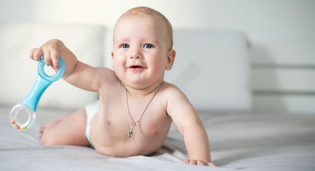 Adorable baby boy in white sunny bedroom. Newborn child relaxing in bed. Nursery for young children.