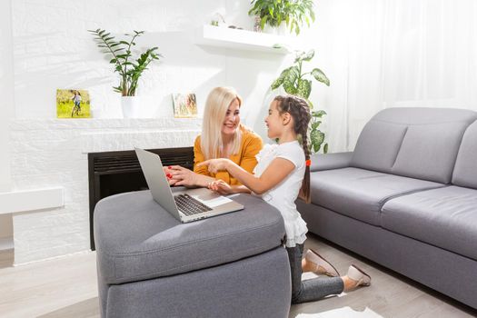 Smiling mother and toddler daughter looking at the notebook indoor. Distance online learning concept. Activities for kids during quarantine.