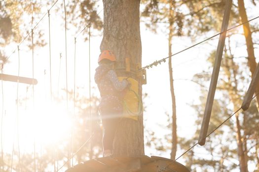 Happy school girl enjoying activity in a climbing adventure park on a autumn day