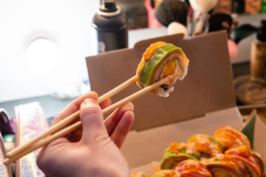 Beautiful young woman eating sushi roll at cafe. Woman eating sushi set with chopsticks on restaurant.